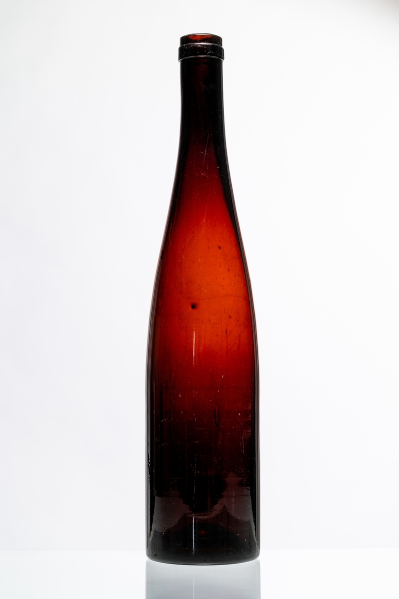 Vinflaska, fransk modell, av röd-brunt glas, avsedd för tillslutning med naturkork. Flaskan tillverkades även i grön färg. Hantverksmässigt tillverkad vid Sunds glasbruk, Jönköpings län. Se vidare Historik.