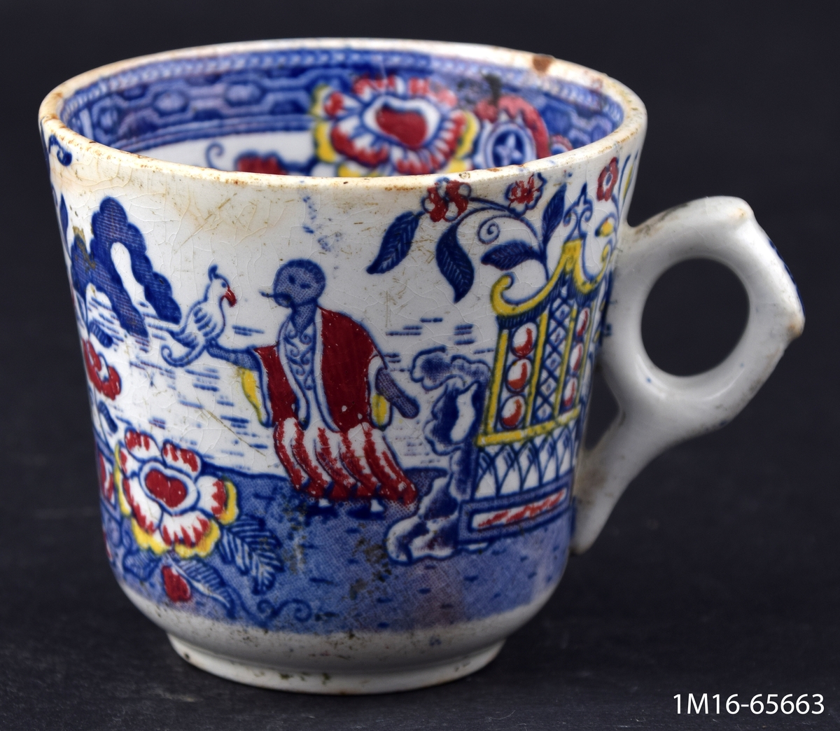 Kaffekopp, dekorerad med kineserier i blått, rött och gult, utanpå, inuti diverse ornament. Ett öra.