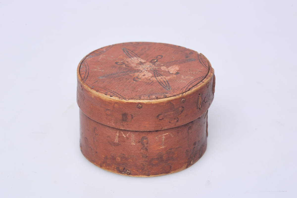 Rund brunmalt dåse av tre som er laget av tjukk høvelspon, endene, endene er sammenfestet med tæger, sviornamentikk på sider og lokk.