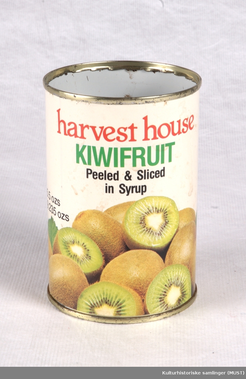 Rund hermetikkboks. Lokk mangler, og det er spor etter boksåpner. Hvit etikett rundt siden med bilde av kiwi. Har inneholdt kiwi-biter i sirup.
