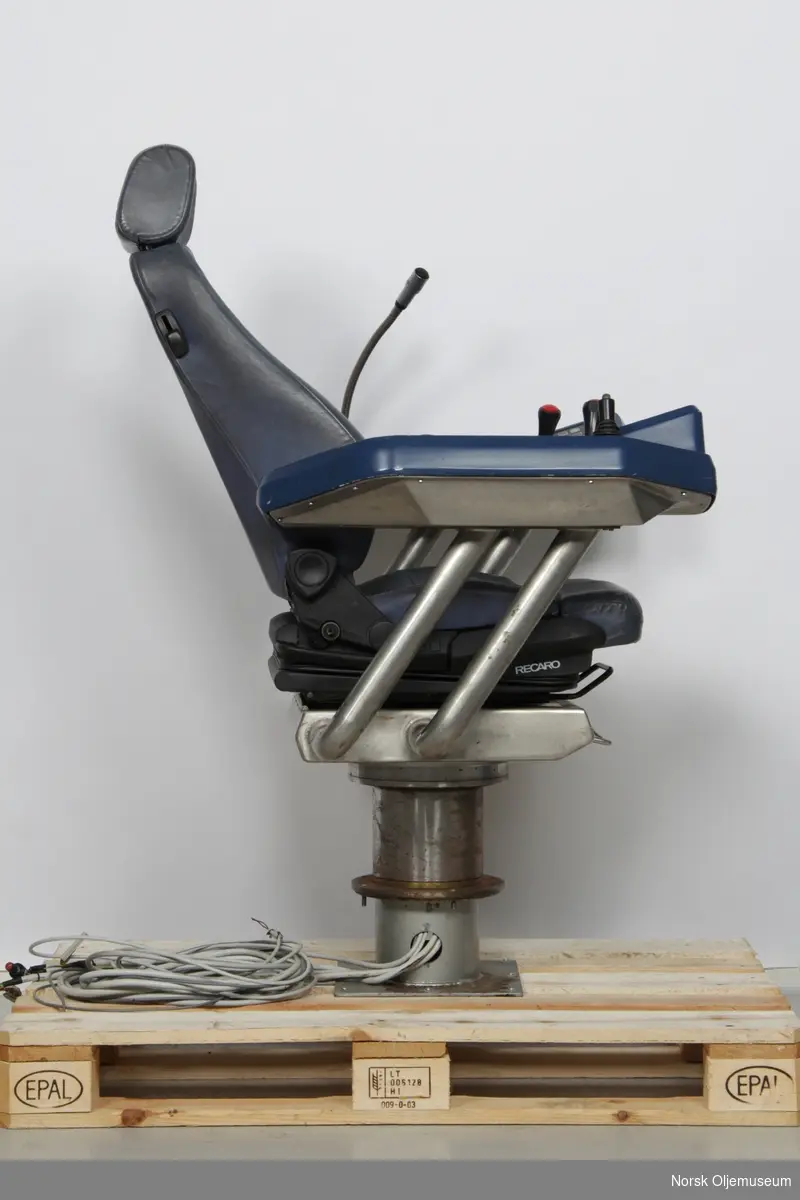 Operatørstol som er utstyrt med styrespaker og knapper for fjernstyring og mikrofon på armlener.