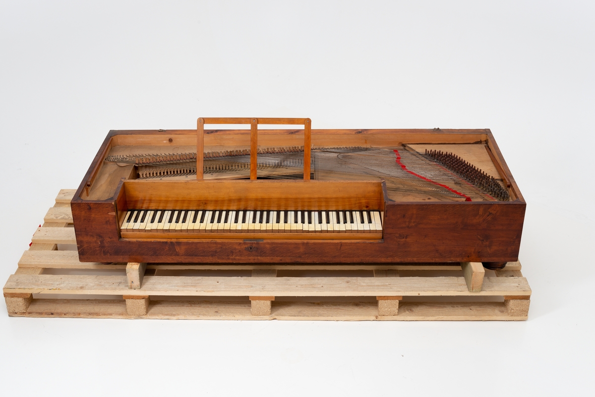 Rektangulært, kasseformet taffelpiano av vanlig type. 6 oktaver, delt klangbunnen til høyre, senere går den over hele instrumentet. Antagelig engelsk eller skandinavisk. Mangler understell. Lokk er løst.