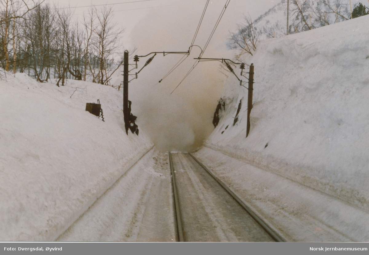 Snørydding ved Fjellberg tunnel ved Haugastøl. En enorm snøskavl hadde bygget seg opp over tunnelmunningen. NSBs Ledningsavdeling trakk til side kjøreledningen hvoretter skavlen ble sprengt med dynamitt, og deretter ryddet med roterende snøplog
