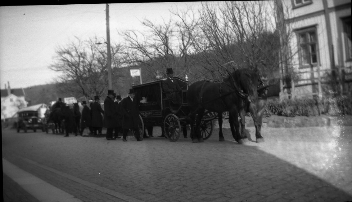 Ett liktåg med vagn dragen av hästar på Brahegatan på väg söderåt. Man passerar den avlidnes hem som skymtar till höger.
