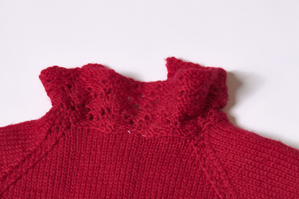 Kjole strikket i rødt ullgarn. Overdelen er glattstrikket, mens skjørtet er en form for kunststrikk. Kjolen har bred fald nederst, og har muligens vært justert etter barnets høyde. 