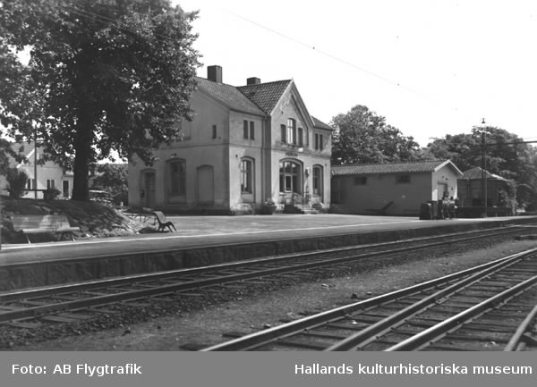 Exteriörbild av järnvägsstationen i Heberg med magasin, perrong parkbänkar och järnvägsspår.