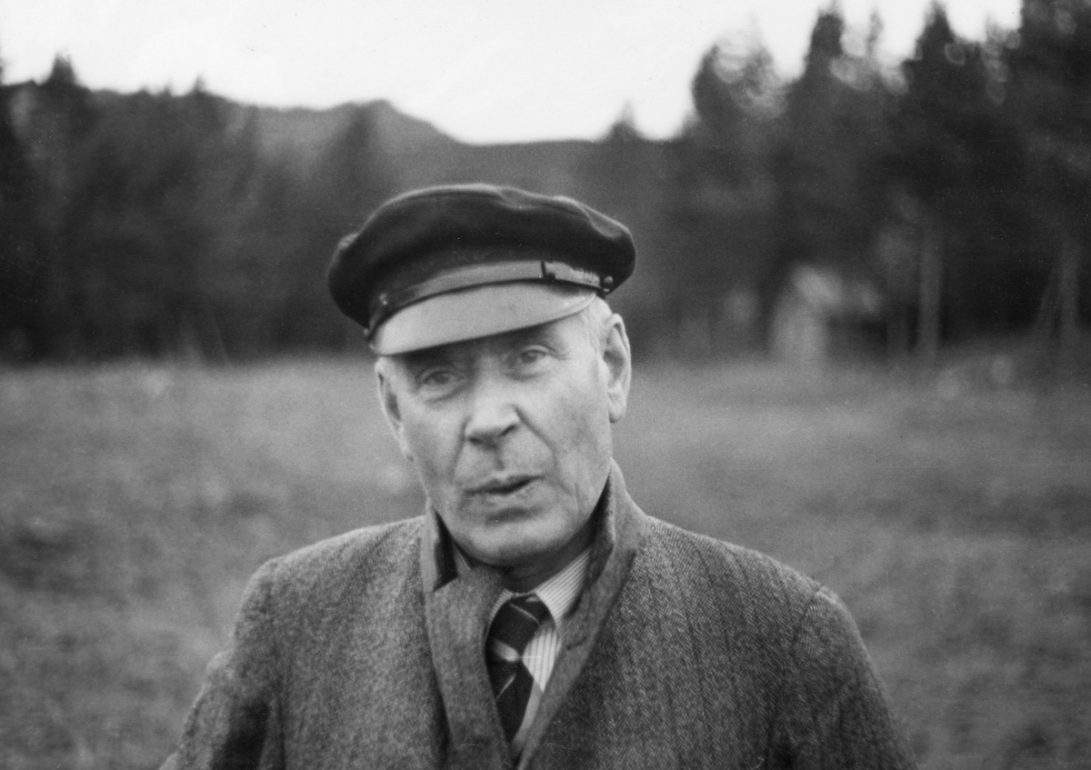 Portrett av Halstein Sjølie (1876-1942), bruker på den store jord- og skogeiendommen Øvre Sjøli i Ytre Rendalen, Hedmark. På dette tidspunktet var Sjølie cirka 61 år gammel. Han var kledd i en grå frakk med oppbrettet krage og stripete skjorte med slips. På hodet hadde han ei lue med blank skygge.