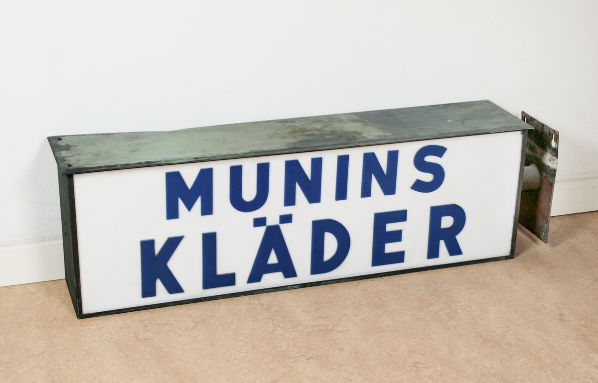 Reklamskylt för affären "Munin kläder" i Borås. Rektangulär med väggfäste på ena sidan. På var sida text i blått: "MUNIN KLÄDER", mot vit botten av plexiglas. Inom hölje av grönmålad järnplåt. Insidan med belysning. Proveniens Munin kläder, Borås.

Funktion: Att fästas på fasadvägg