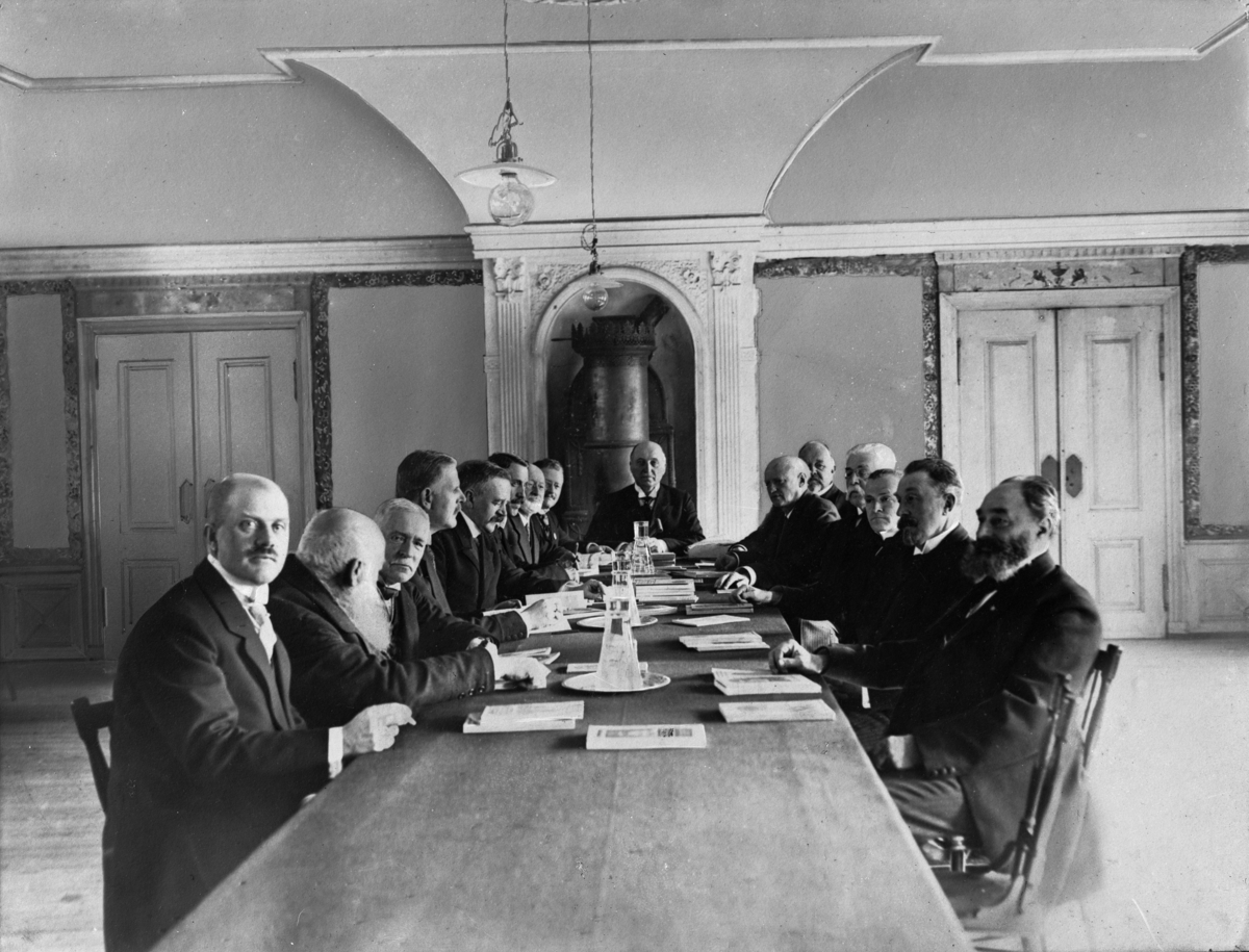 En gruppe menn rundt et stort bord. Et møte, sannsynligvis i sammenheng med 
Norges Jubileumsutstilling 1914, i Frognerparken
