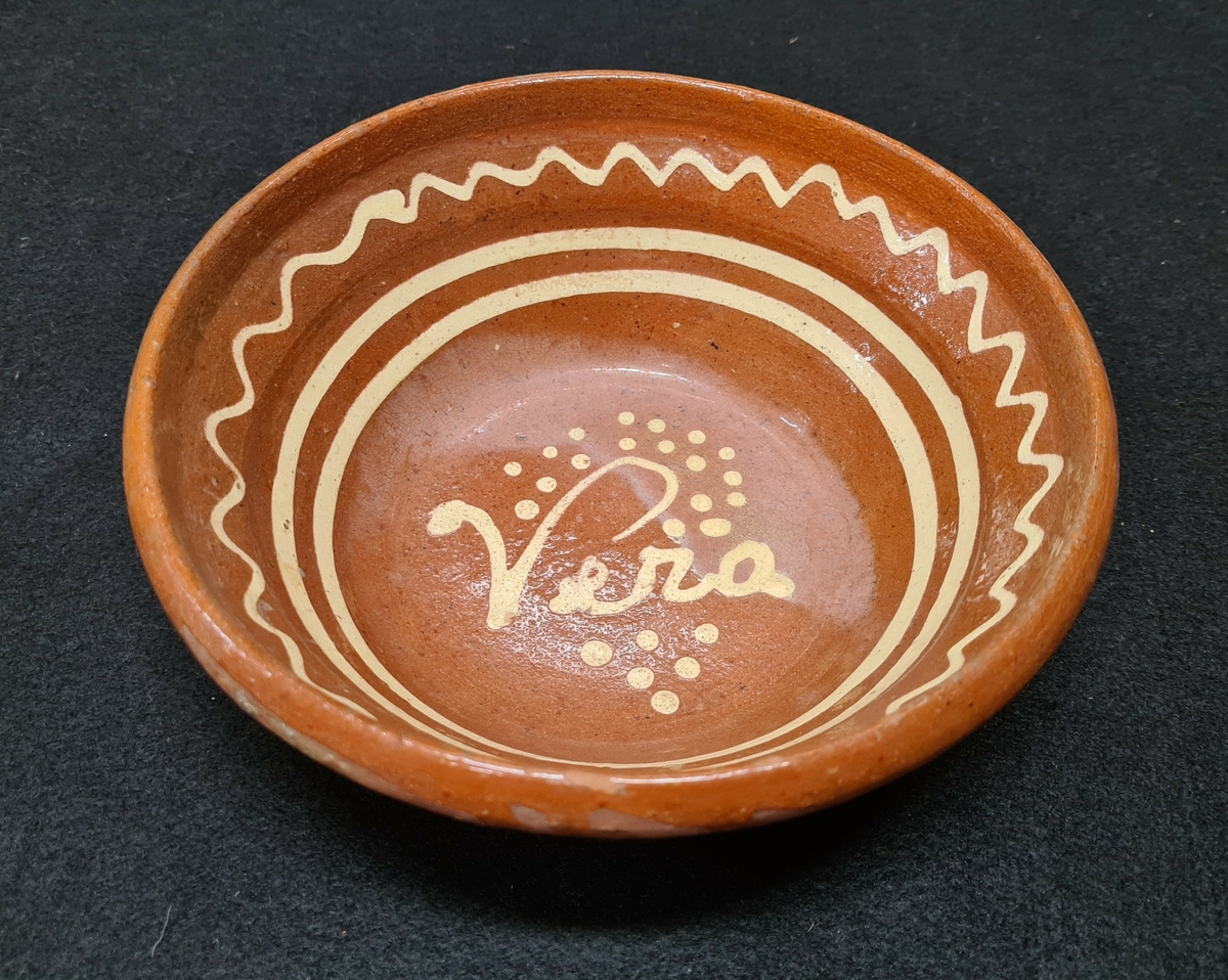 Brunglaserad lerskål med dekor med piplera i ränder och namnet Vera i botten.

Denna skål fick Vera Haij av krukmakare Eriksson när hon var praktikant i krukmakeriet 1935.