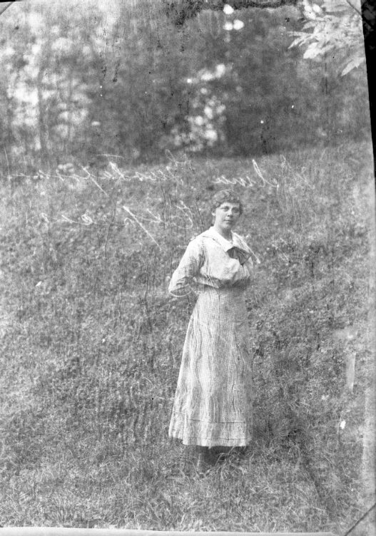 Porträtt av en kvinna som står med händerna bakom ryggen på en gräsmatta.