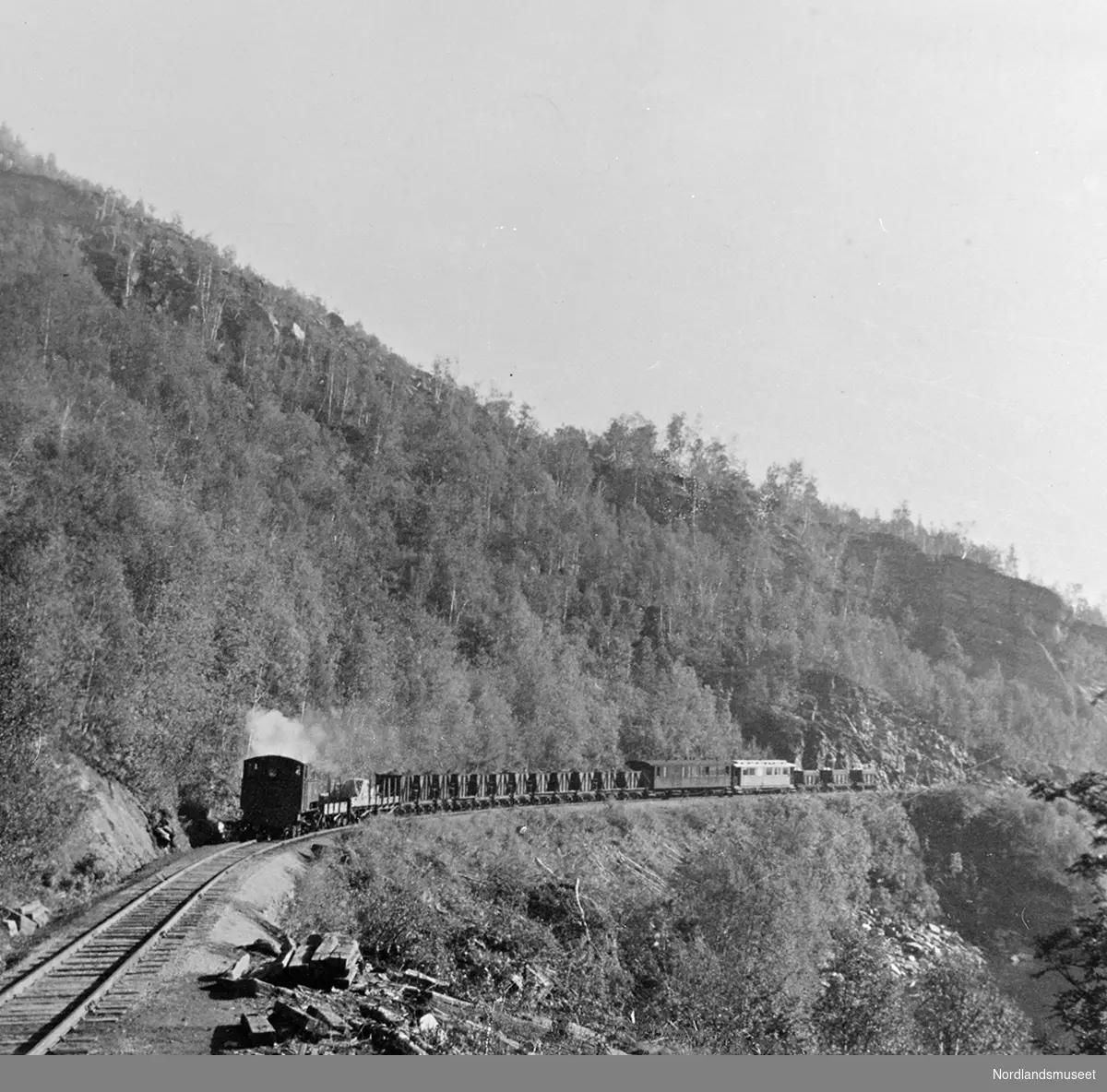 Jernbanelinje og et tog, fra Sulitjelmabanen. Togsettet har to passasjervogner og en rekke kisvogner.