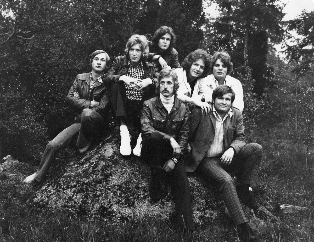 Gruppbild på sju män sittandes på en sten i en skog.