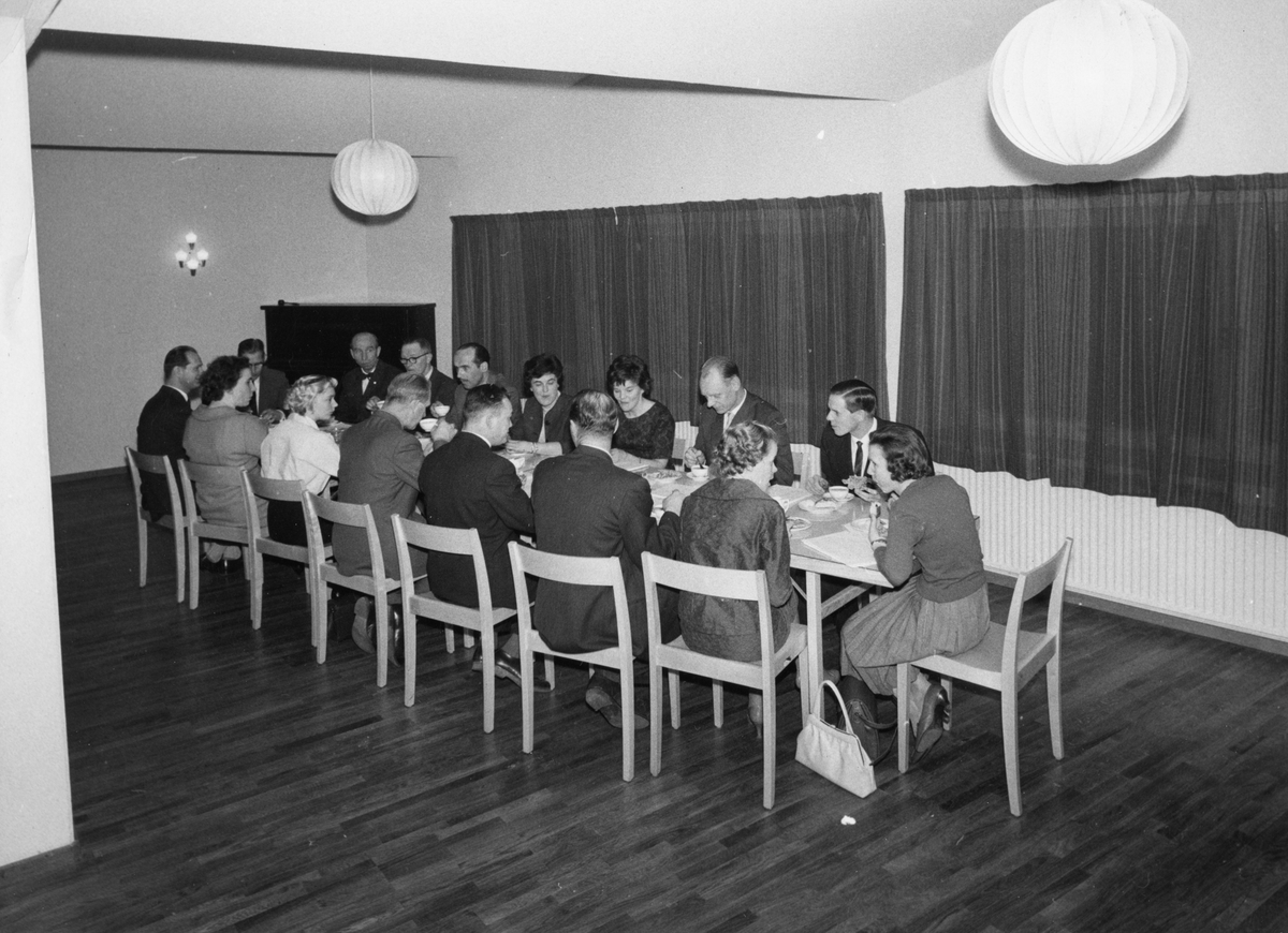 16 personer sitter runt ett långbord och äter.