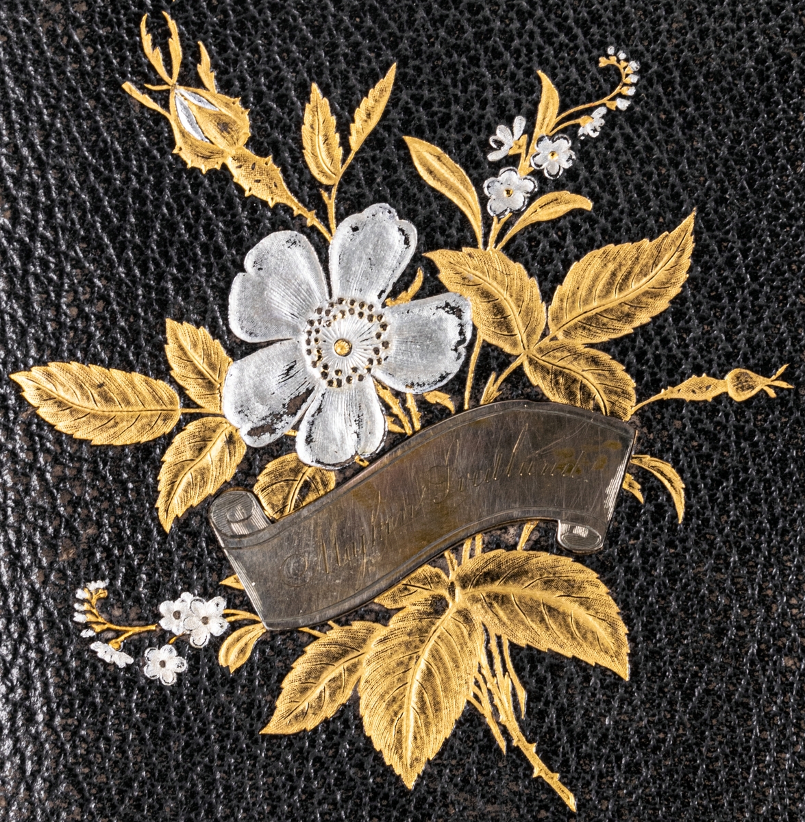 Fotoalbum, svart läder. Dekoration: blombukett med förgyllda blad och försilvrade blommor och namnskylt Majken Svedlund.