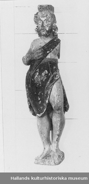 Skulptur föreställande Johannes Döparen, från altaruppsats. Johannes i en face står med ett stycke topografi. Vänster ben något lyft med knät utåtböjt. Vänsterarmen saknas. Högerarmen lyft och böjd så att handen ligger mot mellangärdet. Iklädd djurhud (fäll) med axelband över vänster axel. Djurhuden slutar ovanför midjan, i övrigt bar överkropp. Bär kort skägg och långt lockigt hår. Ovanpå huvudet en vulst. Karaktäristiskt är den extrema kulmagen. Färgbeskrivning: Ansikte: fragment hudfärg och rött, skägg skulpterat och målat i brunt. Hår: brunt, fragment av grått finns på bakhuvudet. Överkropp: hudfärg. Klädedräkt: fällen är brun och grön med röd insida, spår av förgyllning finns liksom fragment av försilvring på midjebandet (fållen, kanten som fällen avslutas med). Ben: hudfärg. Arm: hudfärg. Topografi: grön. / Stefan Hammenbeck 800624 Tillverkning 1650 ca.