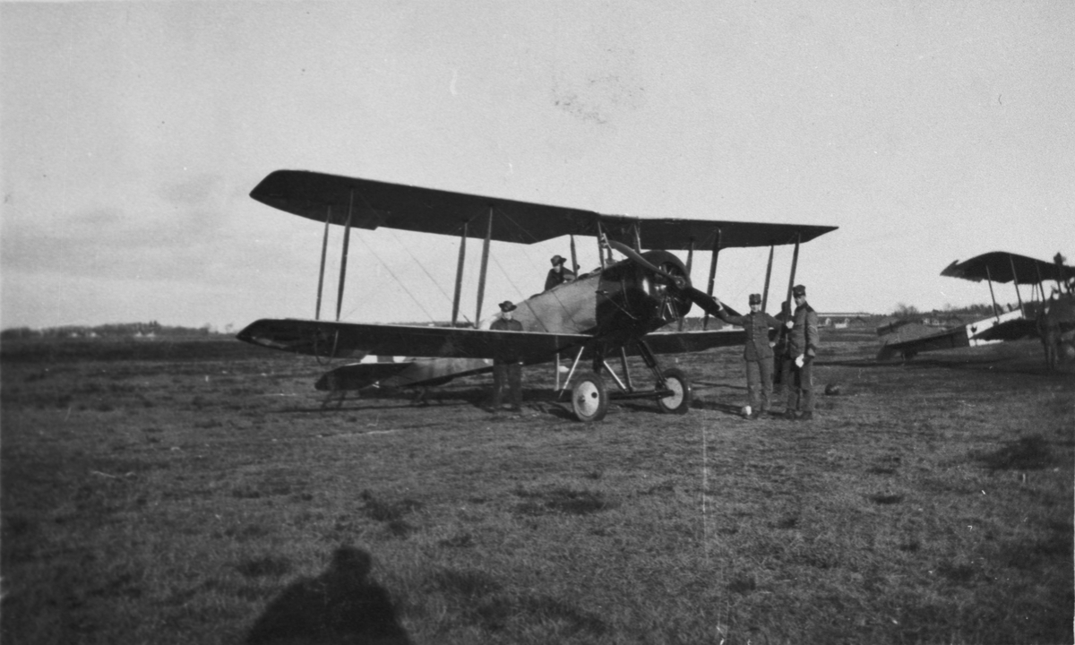 Flygplan Sk 3 Avro 504K ståt på flygfältet på F 5 Krigsflygskolan i Ljungbyhed. Militärer kring planet.