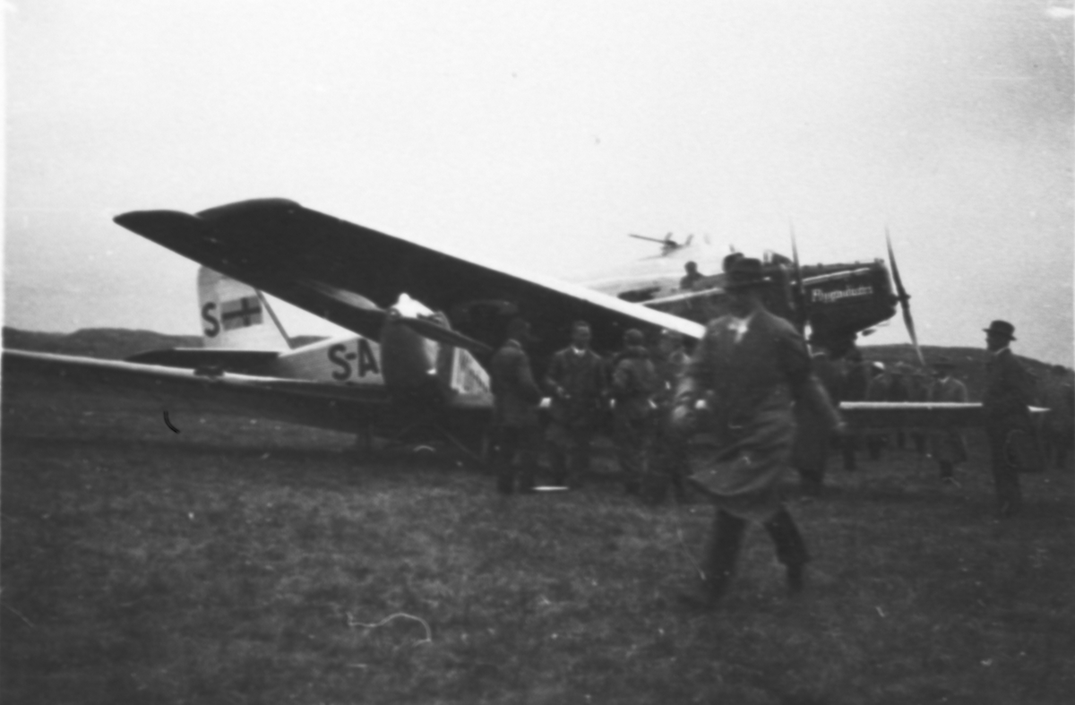 Civilregistrerat flygplan Junkers K 30c tillhörande Svensk flygindustri står på ett flygfält. En folksamling står vid flygplanet. Förmodligen flygplan S-AABF.