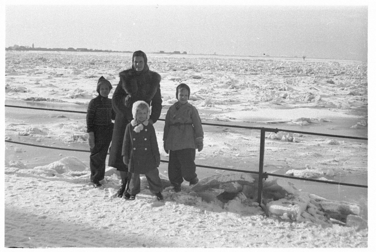 Kvinne med tre barn, fotografert foran en islagt innsjø eller elv.