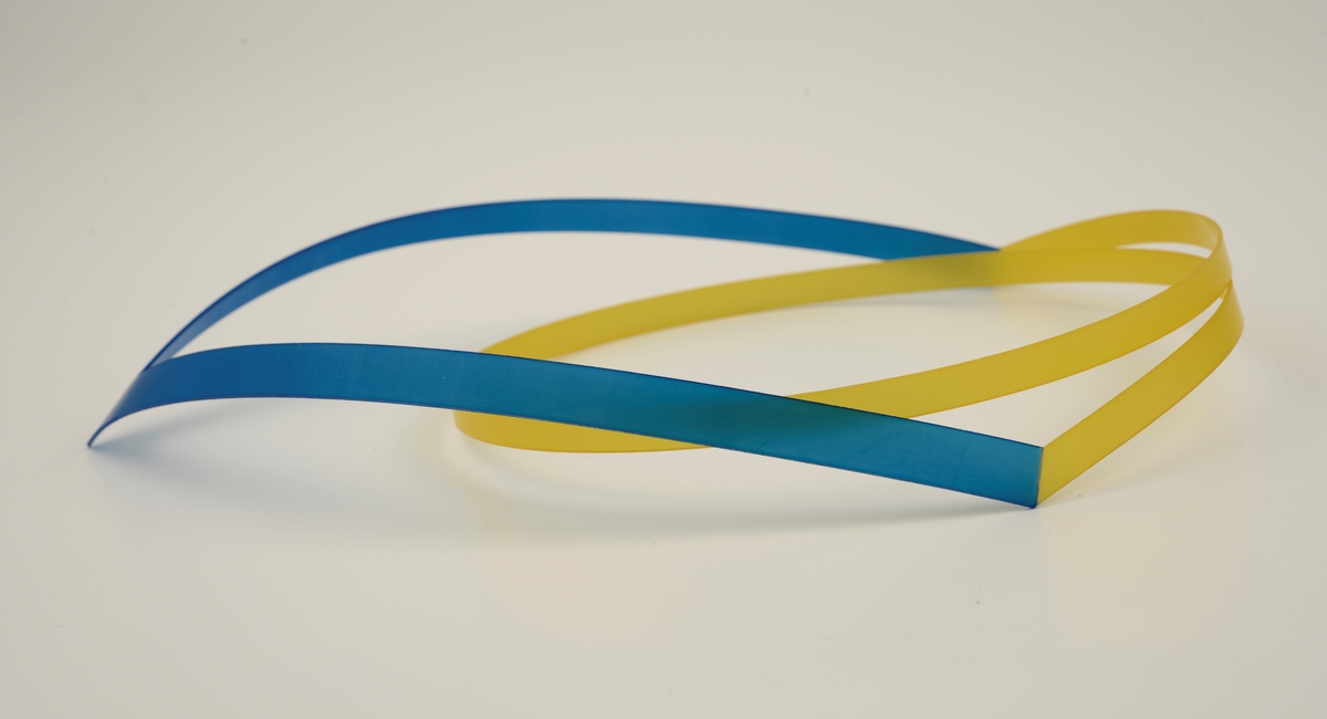 Halssmykke laget av stive nylonbånd som er cirka 1 cm brede. Foran er det et v-formet bånd i blå nylon, til dette er det festet et gult bånd som slynger seg i en spiral.