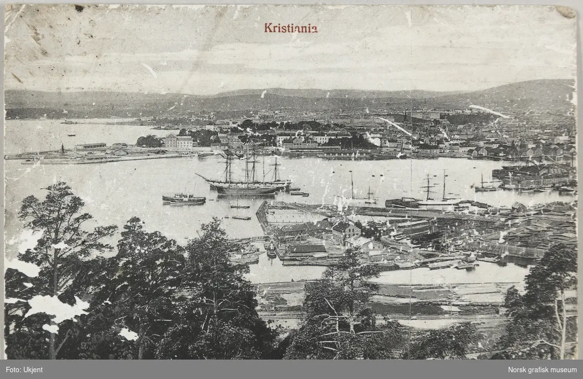 Postkort med bilde av Oslo havn fra Ekebergåsen. Noen store seilskuter og mindre dampbåter ligger til kai.