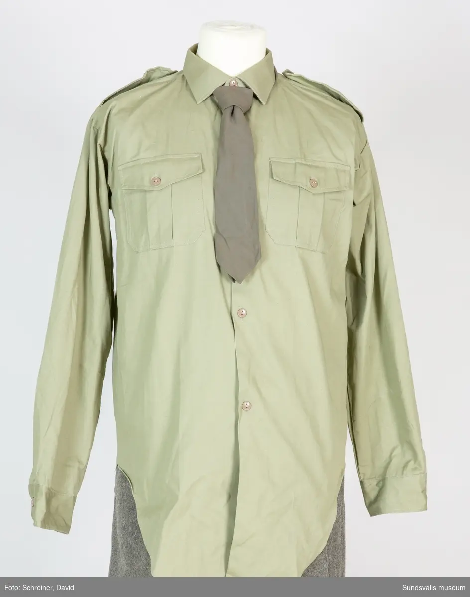 Grön skjorta med två påliggande bröstfickor. Knappslå med sex knappar.
