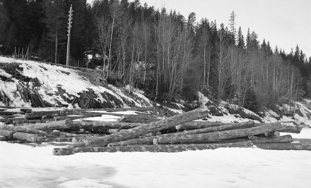 Tømmerleveranse ved fløtingsvassdraget Glomma like sør for Evenstad i Stor-Elvdal i Hedmark.  Fotografiet er tatt i april 1932.  Det viser hvordan et parti med barket fløtingsvirke er veltet utfor en bratt elveskråning på vestsida av elva og ned på den snødekte isen, der det er blitt liggende hulter til bulter.  Dette tømmeret var ikke lett tilgjengelig for eventuell måling, og dersom det ble liggende slik til isen gikk, var det vel også betydelig fare for at det ville ende som en tømmervase, som fløterne ville måtte streve med å få løst opp.  Ifølge en innskrift øverst på bildeflata var dette tømmeret levert til firmaet And. H. Kiær & Co.