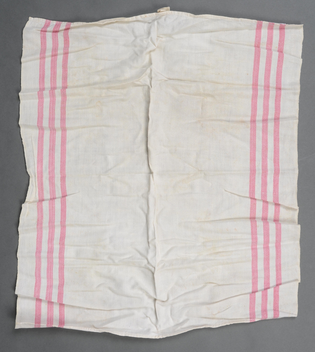 Ubleket vevd håndkle med tre røde striper langs hver langside, påsydde hemper i midten på kortsidene.
