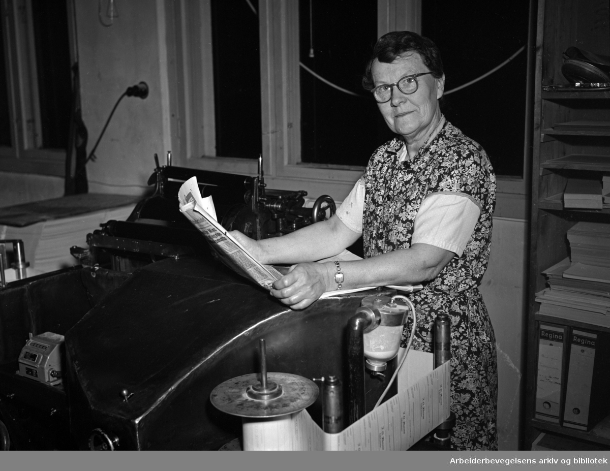 Kvinne leser avis på arbeidsplassen. (Trykkeri) Udatert. Ukjent person. Ca. 1950-1955.