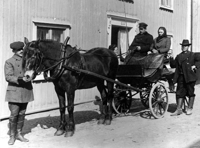 En vagn med en häst står utanför en fastighet. På kuskbocken sitter en man och en kvinna, hon med sjalett och kappan åtdragen - möjligen son och mamma, Oskar och Mathilda. Till höger intill står troligen Mathildas Gustaf Adolf och håller i kuskbocken. Den andra sonen Karl står till vänster och klappar hästen på mulen. Vid dörröppningen på andra sidan vagnen står sannolikt Karls hustru Anna Wilhelmina.