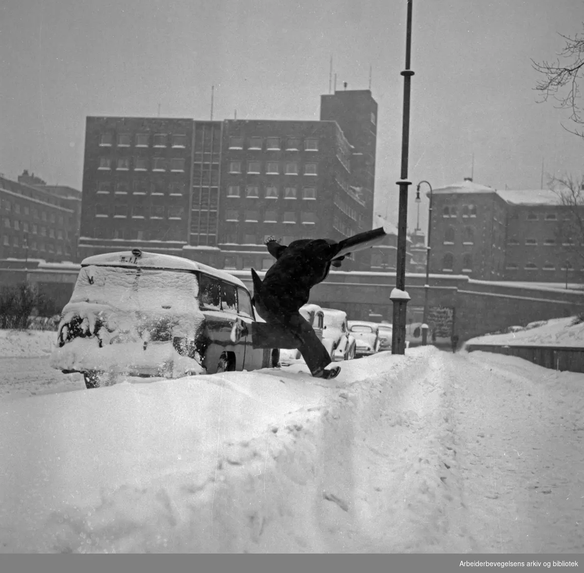 Mann hopper over snøfonn på Arne Garborgs plass. Mars 1954.