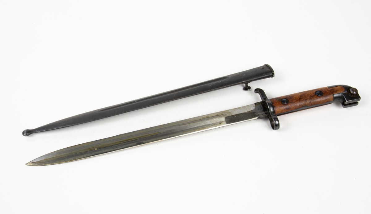 Bajonetten är stridsslipad och förvaras i en knivslida. Bajonetten har trähandtag. Knivslidan är tillverkad i stål.