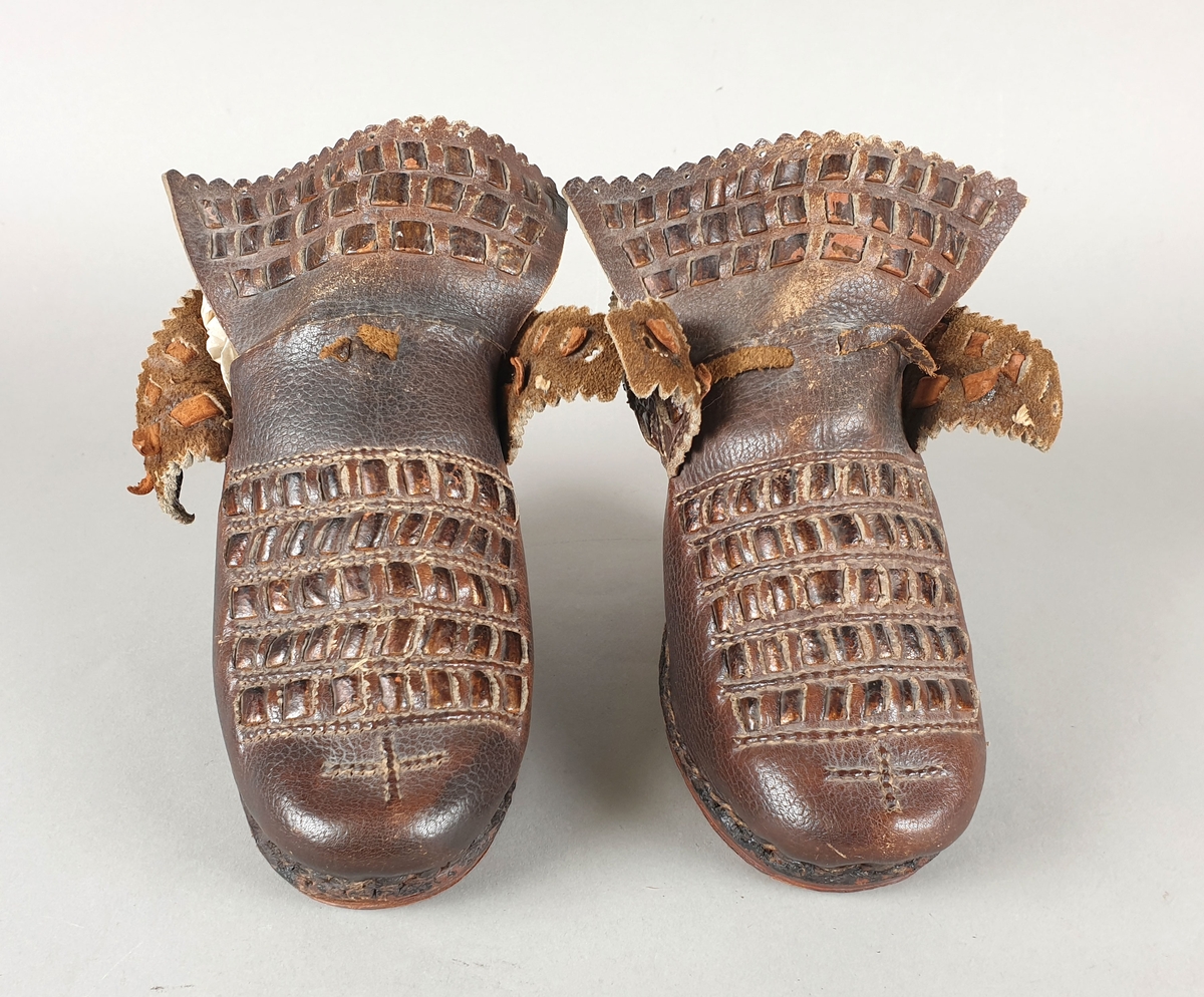 Kopi av sko fra 1700-tallet. Høy hæl og såle av tre. Flettet lær som dekorasjon på over vristen, på tungen og på hælkappen. Randsøm.