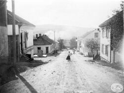 Fotografi i svart-hvitt av Øvrebyen. Fotoet er tatt fra Balchenbakken ned Storgata. I midten av bakken ser vi en kvinne med hatt og svart skjørt. Eller er gaten stille.