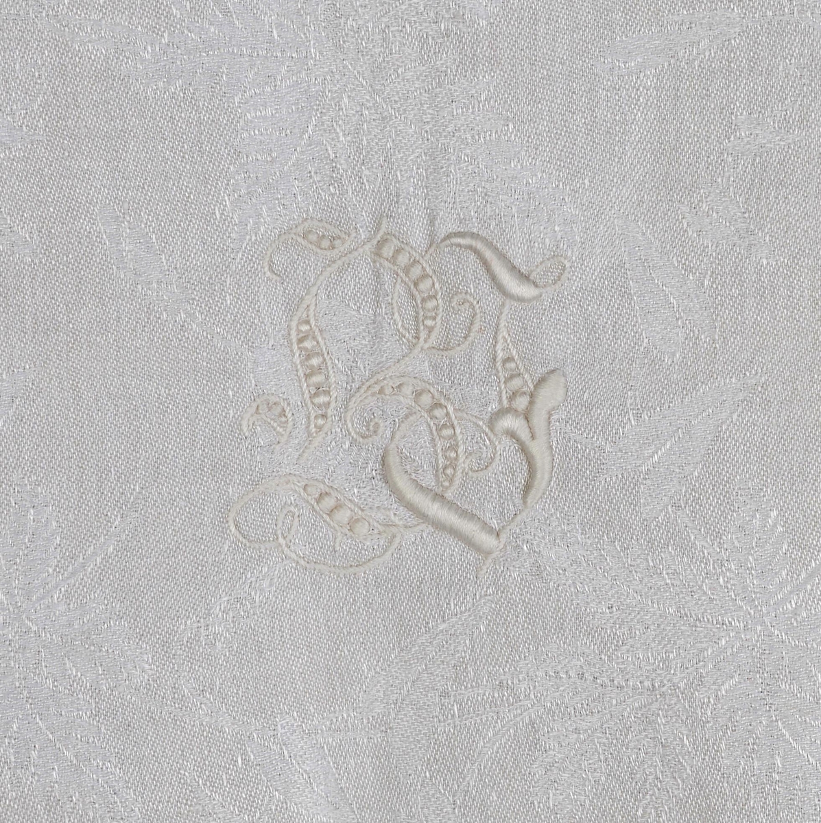 Damaskvevd pyntehåndkle med påsydd dekor av hardangerbroderi. Brodert initialene B i engelsbroderi.