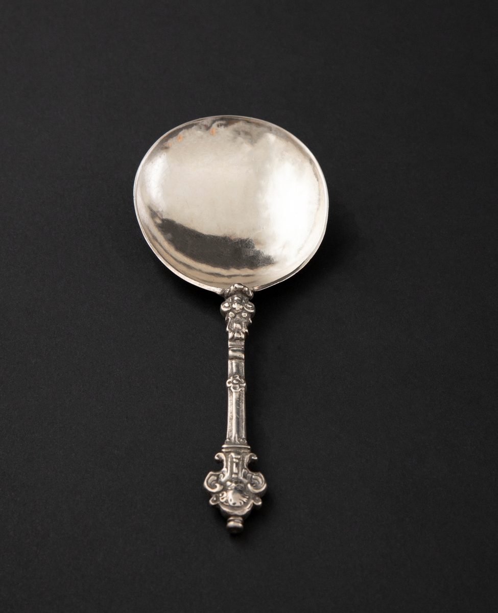 Kjerubskje i sølv med ornamentert skaft og dråpeformet skjeblad. Enden er dekorert med kjerubhoder på begge sider.