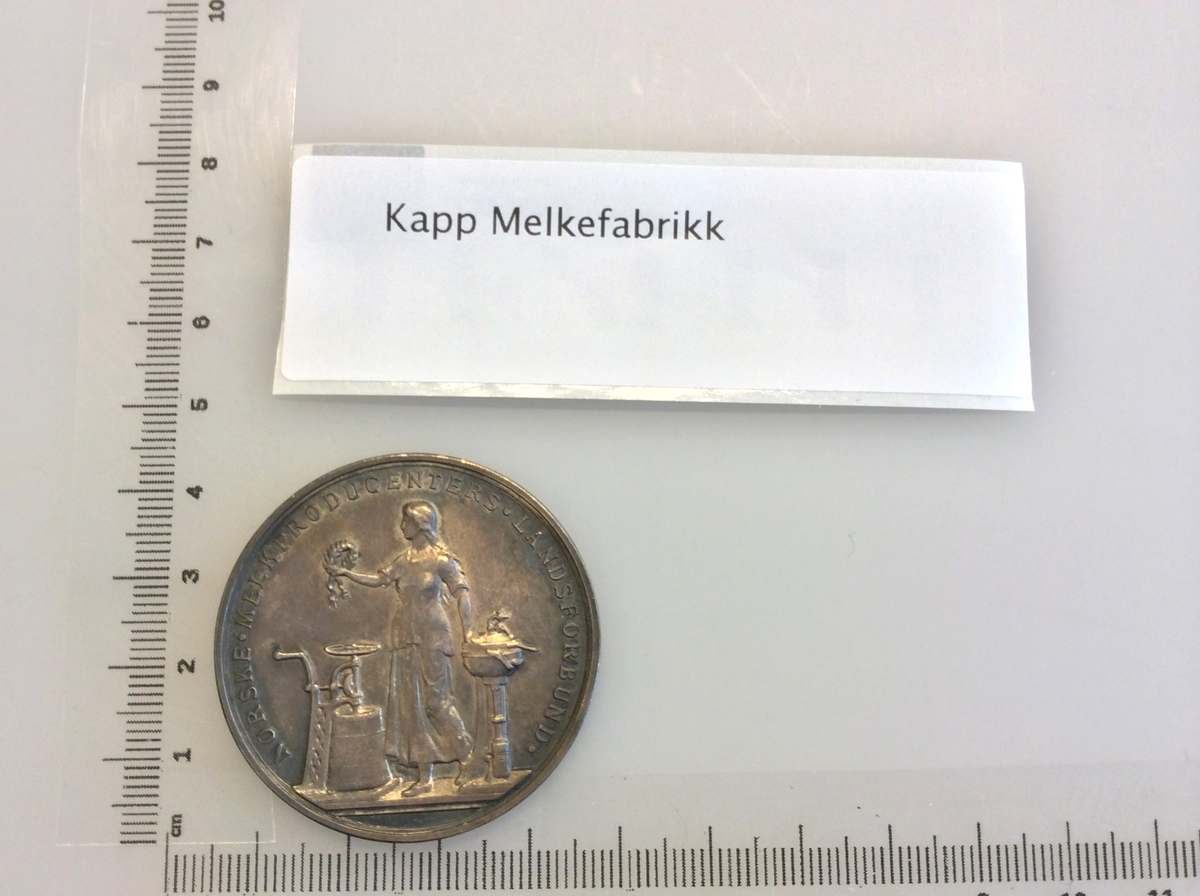 Etui med gråfarget mynt avbildet med en karakter fra gresk eller romersk mytologi på den ene siden og en laurbærkrans på den andre