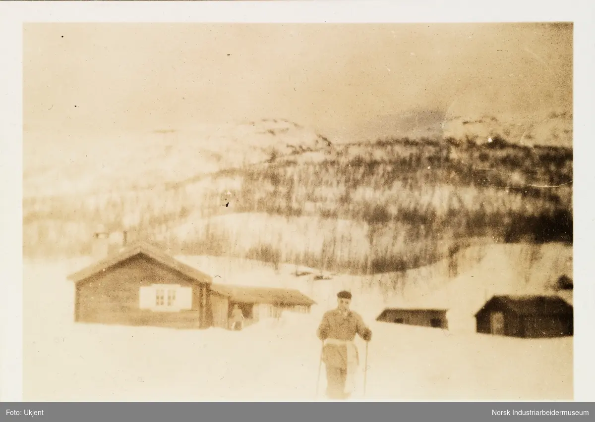 Påsken 1927 på Møsstrond. Mann på skitur, i bakgrunn laftet hytte og uthus
