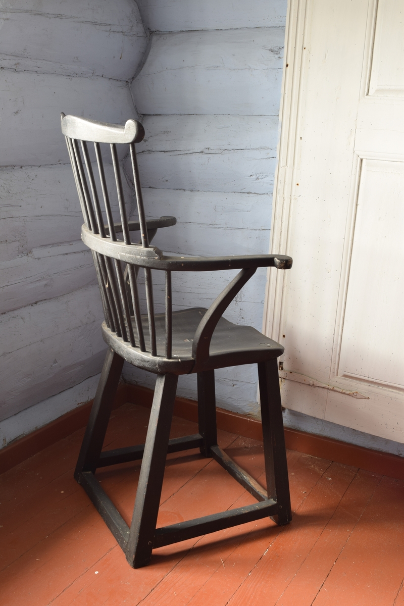 Sortmalt høyrygget stol med dreide ben og spiler i ryggen. formet som en pinnestol med høyere rygg og armlener