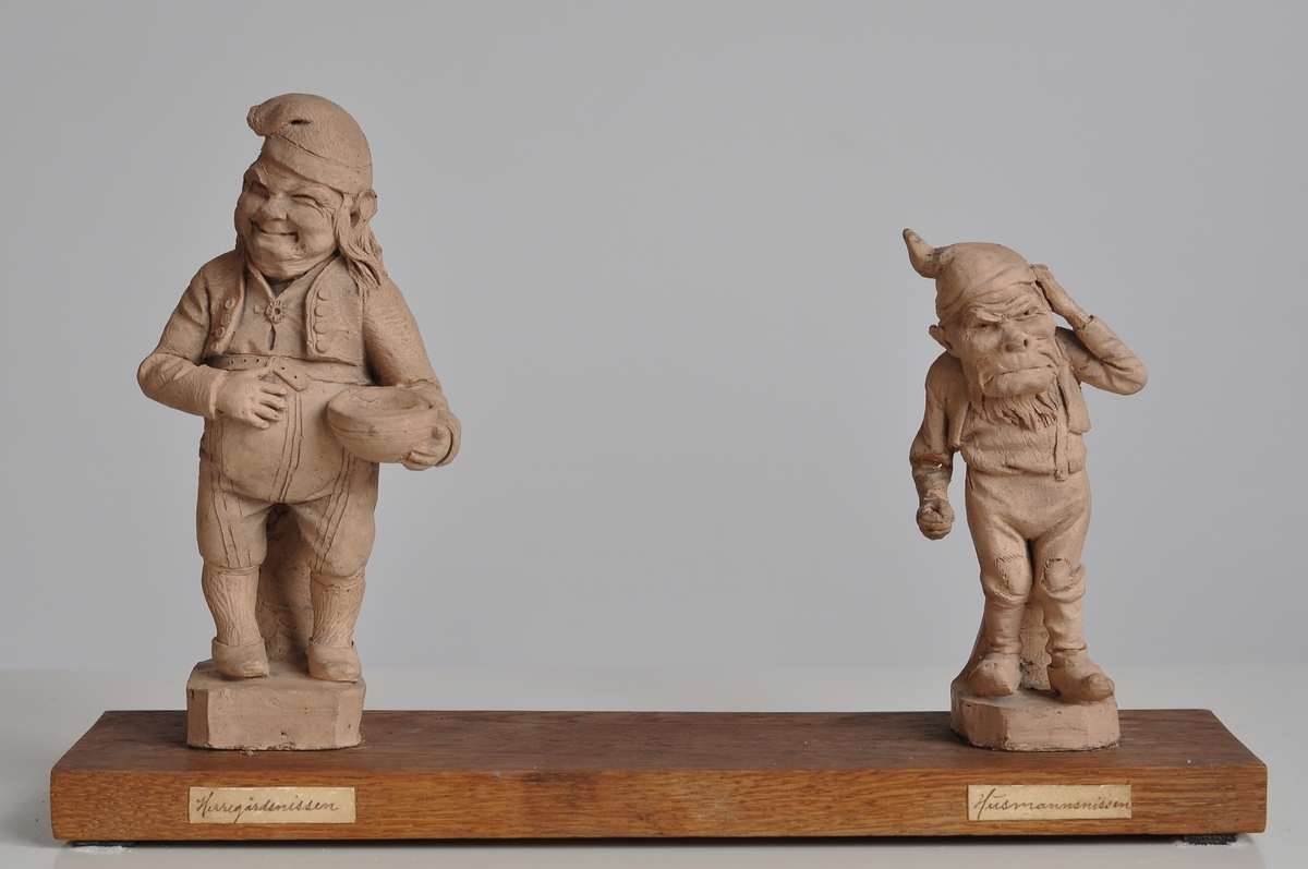 Humoristisk og satirisk skulptur. Gruppering, to små statuetter av gips festet til en sokkel av tre.