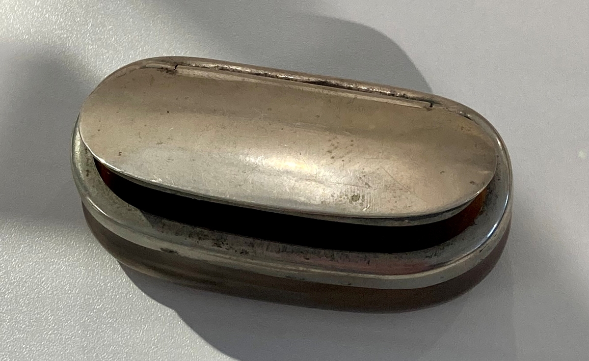 Oval snusdåse av horn, med lokk i metall. (Midt på bildet.)