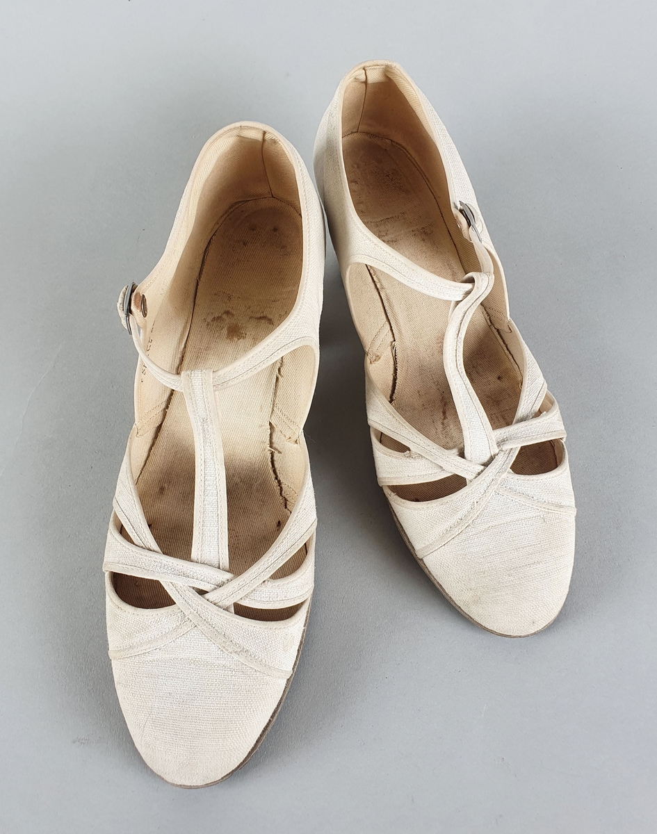 Hvite sandaler av bomullslerret med såle av lær og høye hæler. Spenne på yttersidene.
