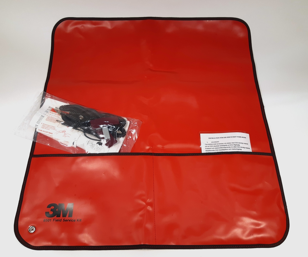 ESD Servicekit, bestående av en ihopvikbar och antistatisk arbetsmatta i röd plast. Samt en oöppnad materielpåse, innehållandes ett handledsband och en jordningskabel med krokodilklämma. Medföljer en instruktionsmanual gällande ESD Servicekit.