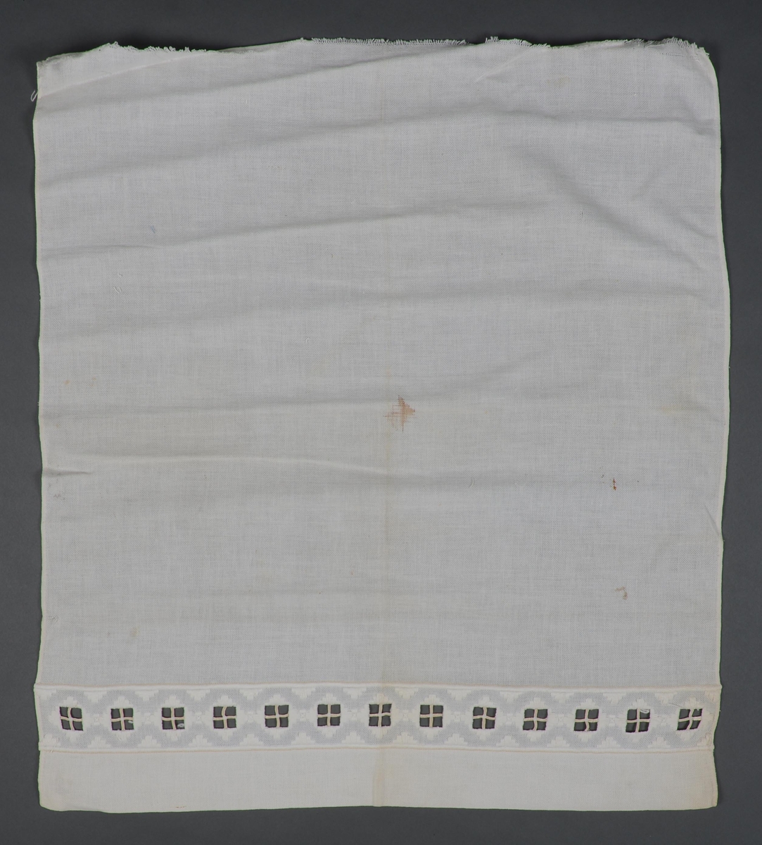 Pyntehåndkle, avskåret, i hvit sultan med bred bord i meget grovt hardangersømmønster sydd med tykt bomullsgarn. Langsidene er brettet inn og sydd til for hånd.