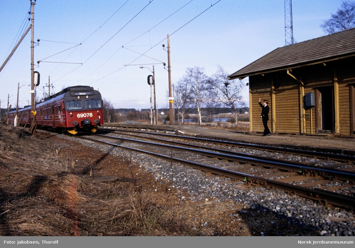 Lokaltog til Moss, tog 127, med motorvognsett type 69 passerer Holstad stasjon på Østfoldbanen. Togekspeditøren står på plattformen