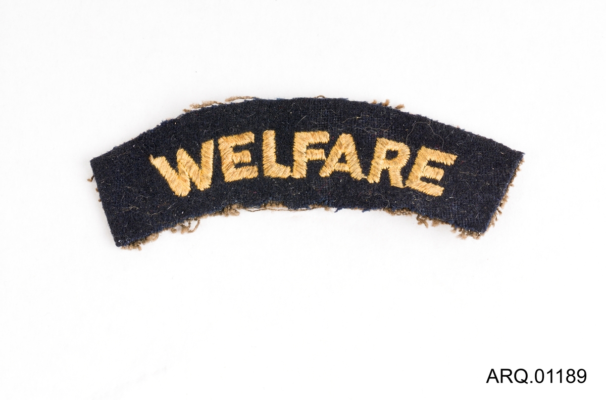 Jakkemerke i tykk filt til å sy på uniformsjakke fra marinen. Svart med skrift brodert med gulltråd.