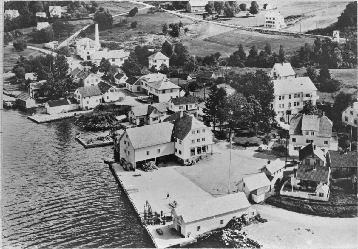 Dampskipkaien i Ølen, ca. 1955. Til venstre i biletet er den gamle butikken ved kaien (her står i dag eit lagerbygg). Til høgre over gata er Forretningshuset (med valma tak), bygd i 1938.