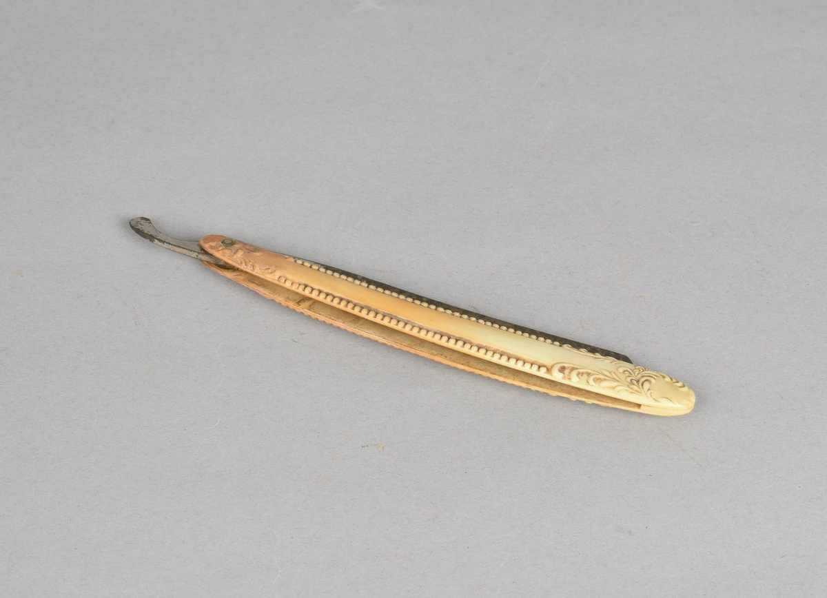 Sammenleggbar barberkniv med skaft i benmateriale med perlesnor og bladforsiring, i todelt futteral av papp kledd med tekstil.