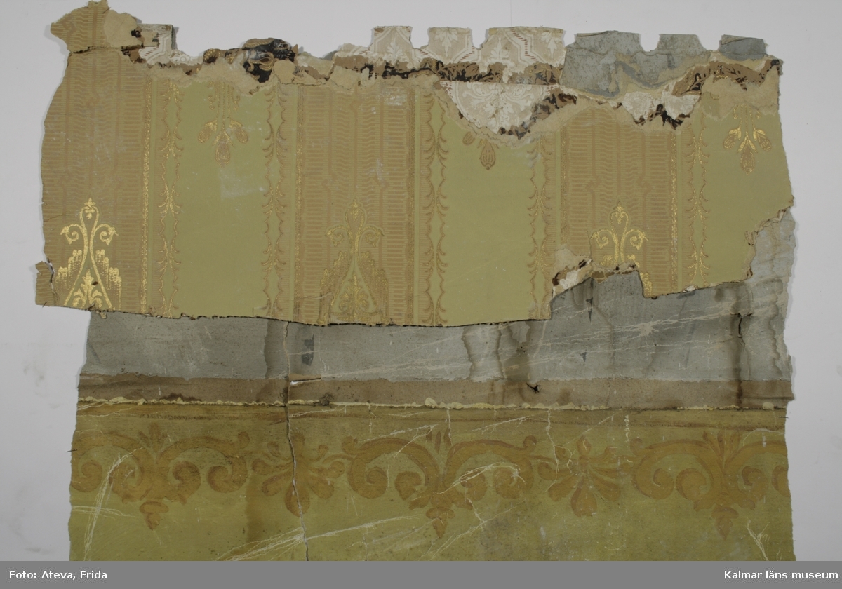 KLM 39925:6:1. Tapet av papper. Ett större väggfält och elva mindre bitar. Målad tapet med grön botten på två tredjedelar och schablontryckt bård i brunt och gult innan övergång till del med målad marmorimitation i grått och grönblått, eventuellt samtida. På de mindre bitarna finns fragment av flera ovanliggande tapetlager med andra mönster, bland annat en bård, bredd cirka 11 cm, med grå drapering och gulbruna rosor och kransar med schweinfurtergröna blad. Närmast ovanpå denna sitter fragment av tryckt tapet med bruna och röda blommor på satinerad beige botten. Ovanpå denna sitter fragment av velourbård i svart och brunt. Över denna en tryckt tapet med svart botten och nästan yttäckande blom- och bladmönster i bruna färger och guld, KLM 39925:6:2. Överst av tapetlagren sitter en tryckt tapet med ljusgrön botten och vissa utsparade ytor. Gulddetaljer i lodräta fältindelningar.