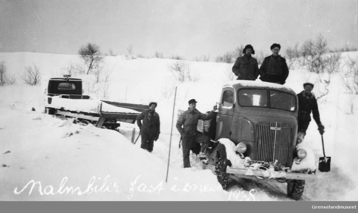Malmbil fast i snøen, 1938. Flere menn med spader står rundt og oppå lastebilen.